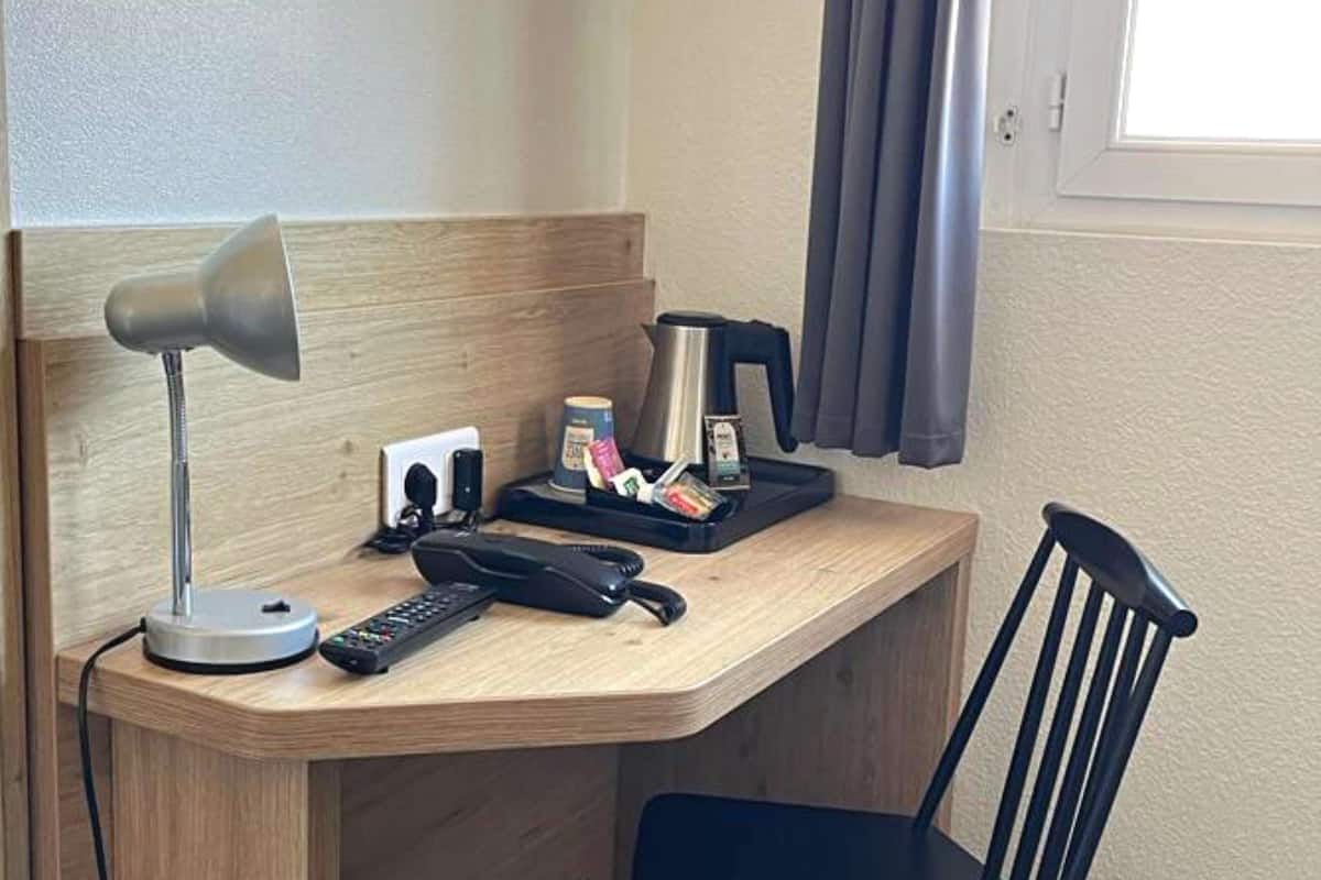 Un escritorio de hotel con una lámpara, un teléfono, una cafetera y una pequeña bandeja con objetos.