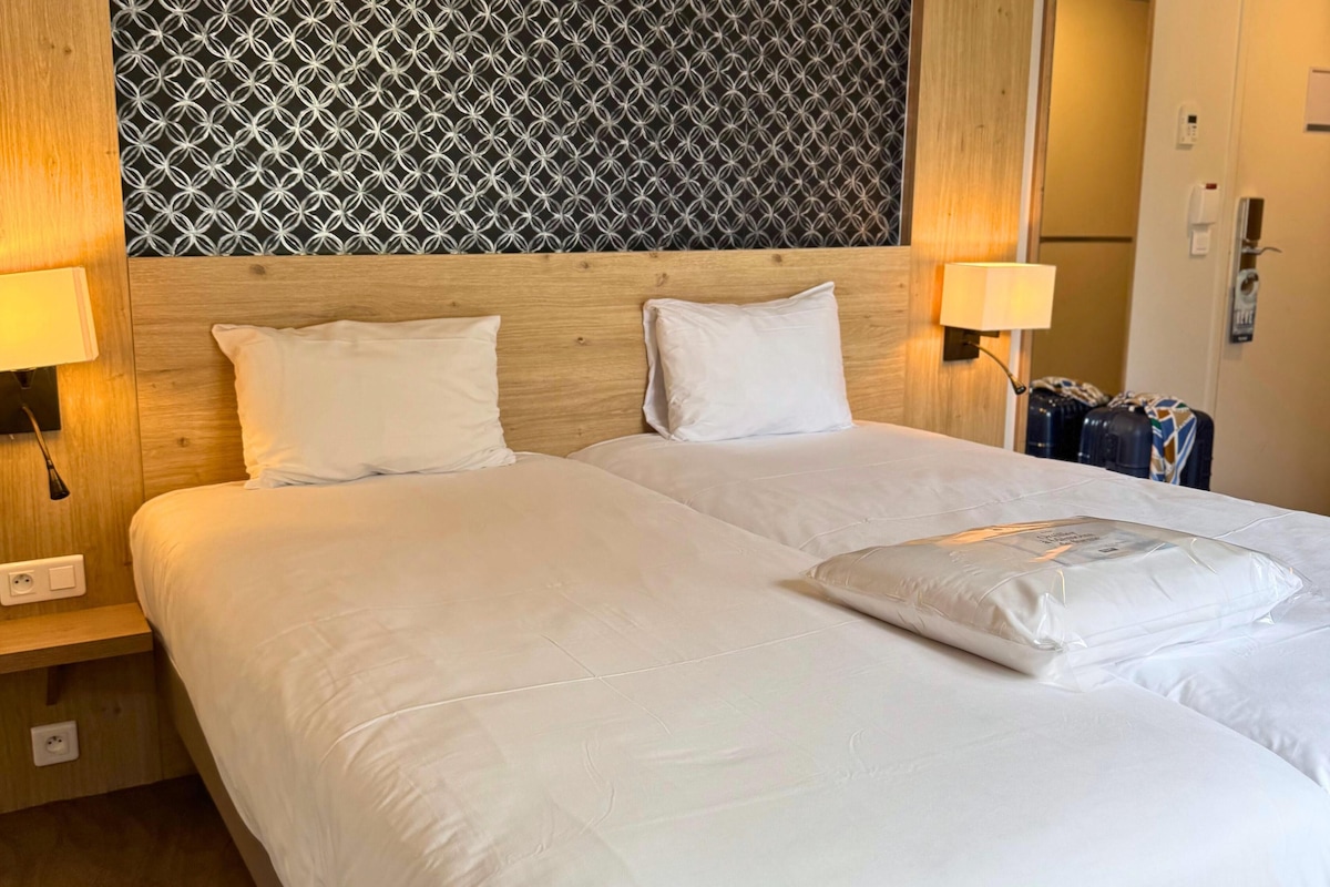 A double bed with white linens, two bedside lamps, and a patterned wall behind.