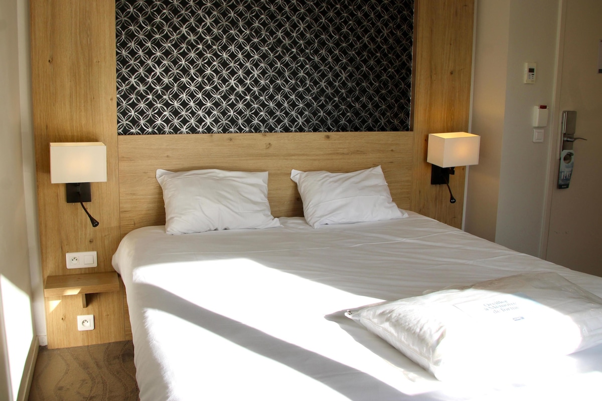 A neatly made bed with white linens, two bedside lamps, and a patterned wall behind the headboard.
