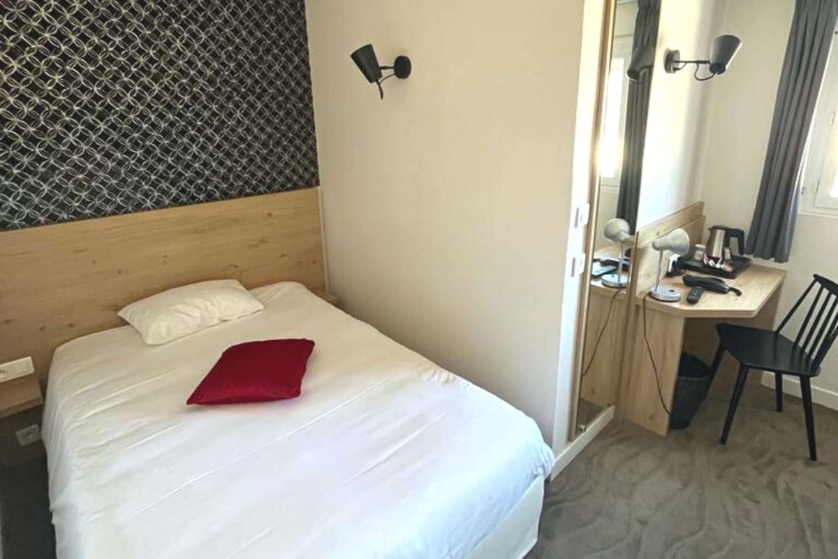 A hotel room with a bed, a desk, a chair, and a mirror.