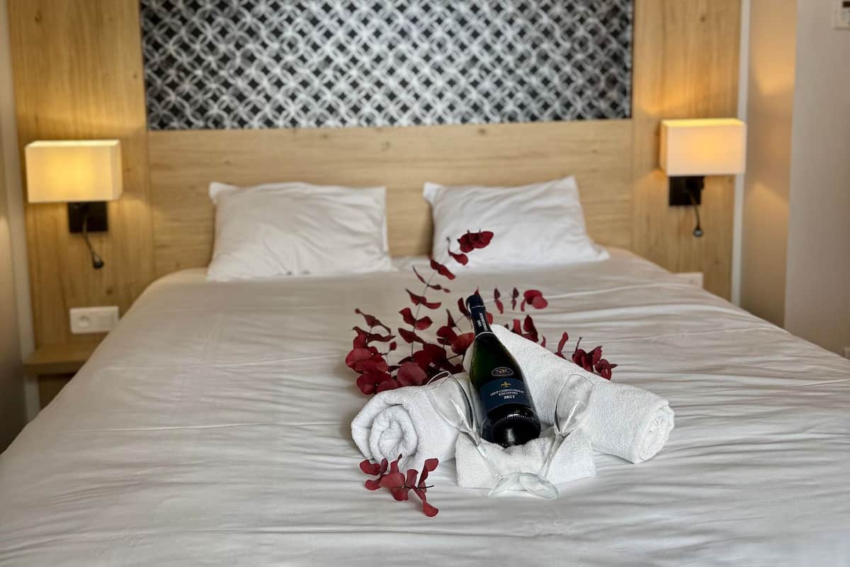 Una cama bien hecha con una botella de vino, una toalla y flores rojas sobre la cama de una habitación de hotel.