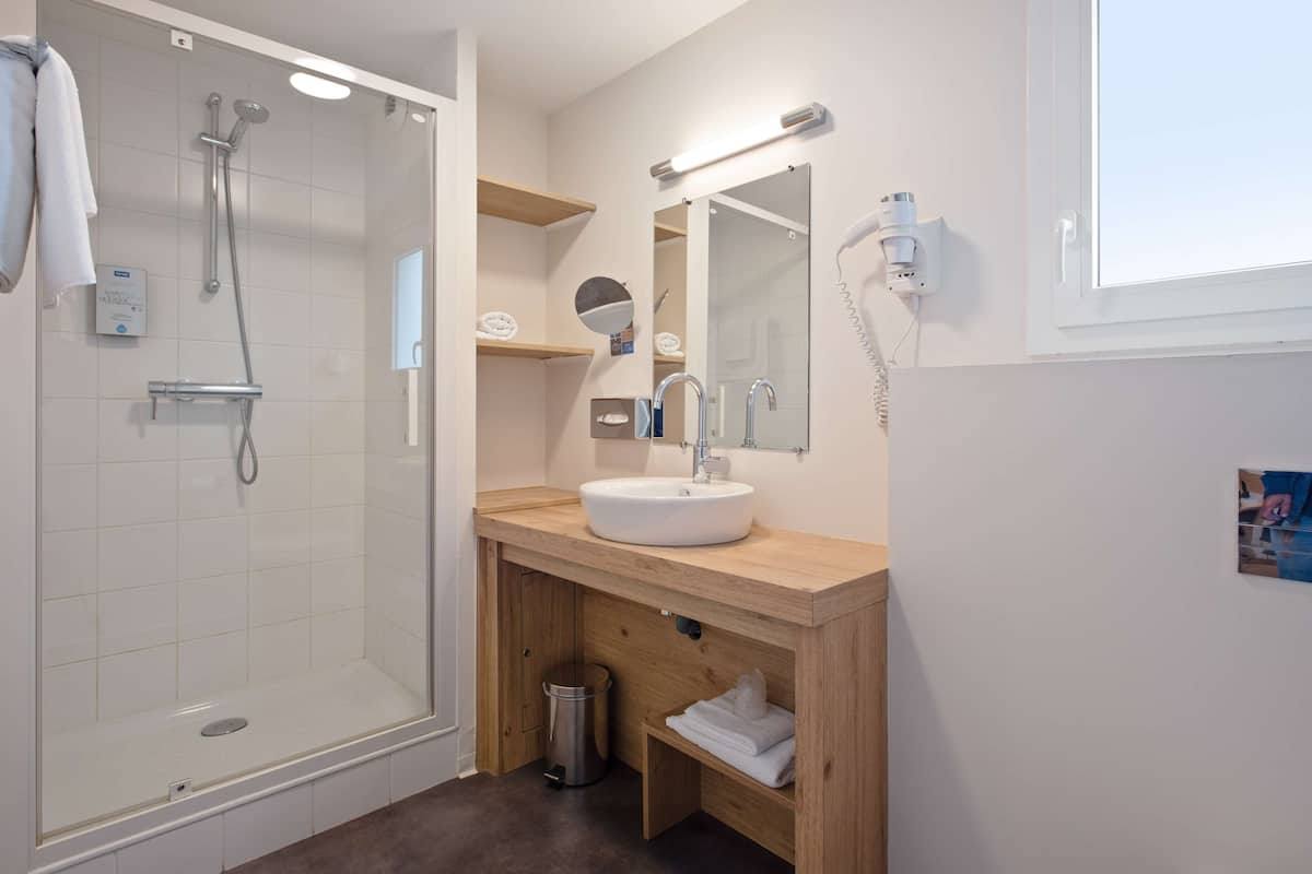 Un baño moderno con ducha envuelta en vidrio, tocador de madera con lavabo y espejo con luz superior.