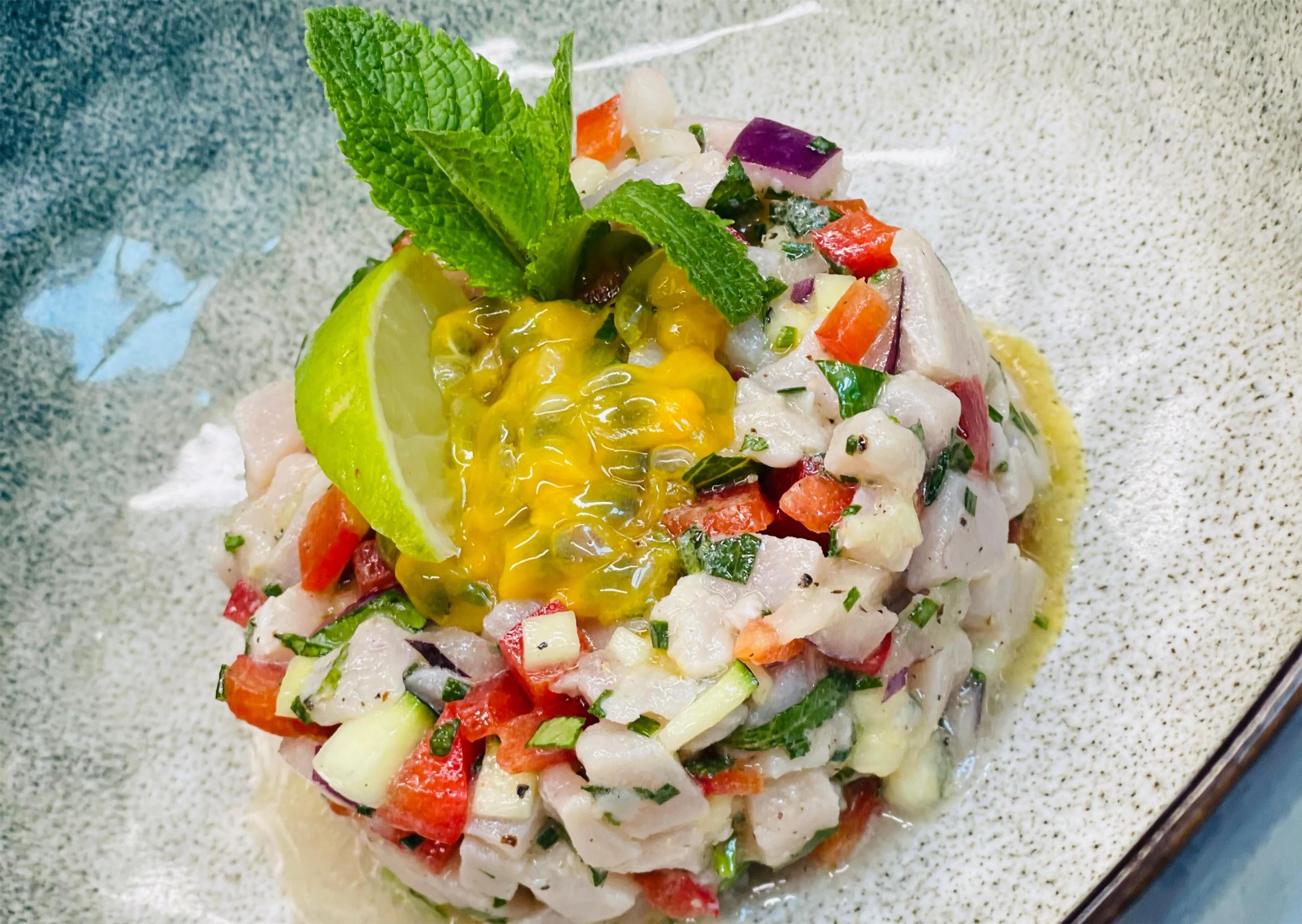 A seafood dish with a lime wedge and mint garnish on a speckled ceramic plate.