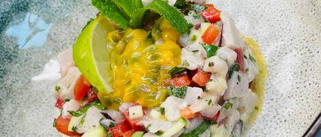 Un plato de mariscos con un gajo de lima y ramitas de menta sobre un plato de cerámica con manchas.
