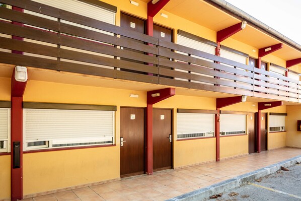 A building with a yellow facade, multiple closed shuttered windows, and a red and brown balcony structure. - Hotel Campanile Lisbon South - Setubal (Setubal)