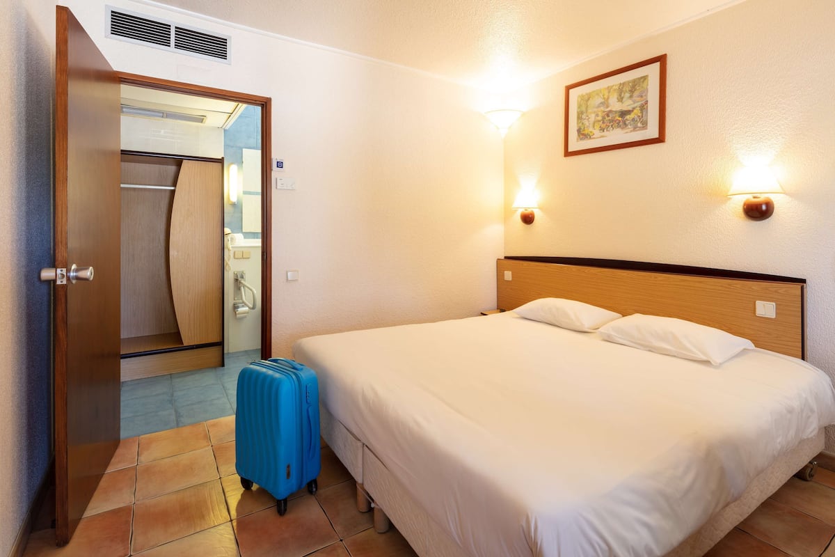 Una habitación de hotel con una cama, una maleta azul, un cabecero de madera y un cuadro en la pared.