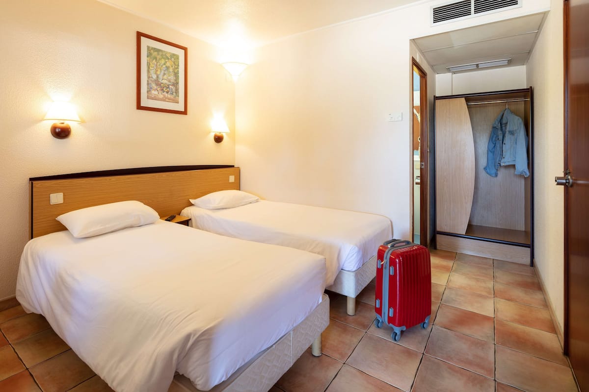 Una habitación de hotel con dos camas individuales, una maleta roja y una zona de ducha.