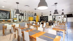 Un espace repas moderne avec plusieurs tables et chaises, une cuisine en arrière-plan et un menu écrit à la craie.