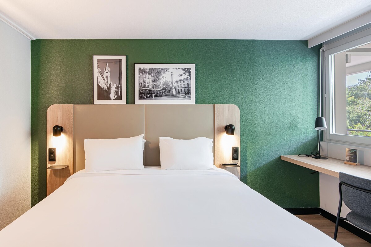 Habitación de hotel con una cama grande, dos mesitas de noche, un escritorio y dos cuadros en la pared.