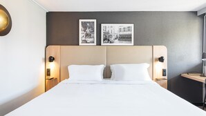 Una camera d'hotel con un letto grande, due comodini con lampade, una testiera in legno e due fotografie incorniciate appese al muro.