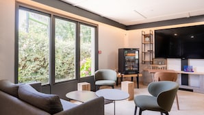 Una hall moderna di un hotel con ampie finestre, zone relax, un frigorifero fornito di bevande e una televisione a schermo piatto.