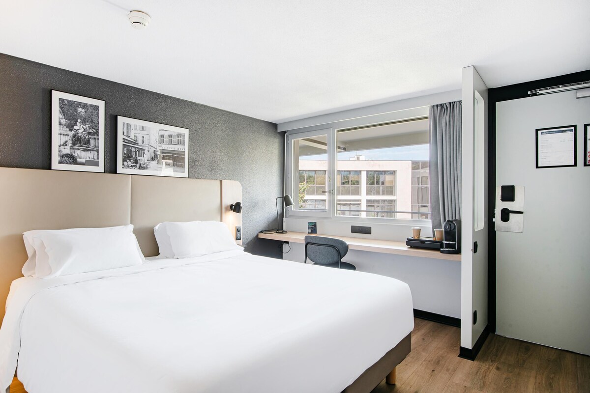 Habitación de hotel con una cama grande, un escritorio y una ventana con vista a edificios.
