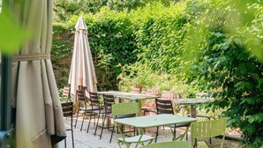 Un patio esterno con tavoli e sedie, immerso nel verde.