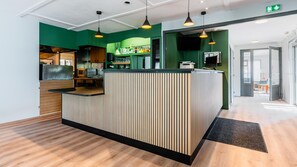 A reception area with a counter, green walls, and a wooden floor. - Campanile NATURE - Vannes (Vannes)
