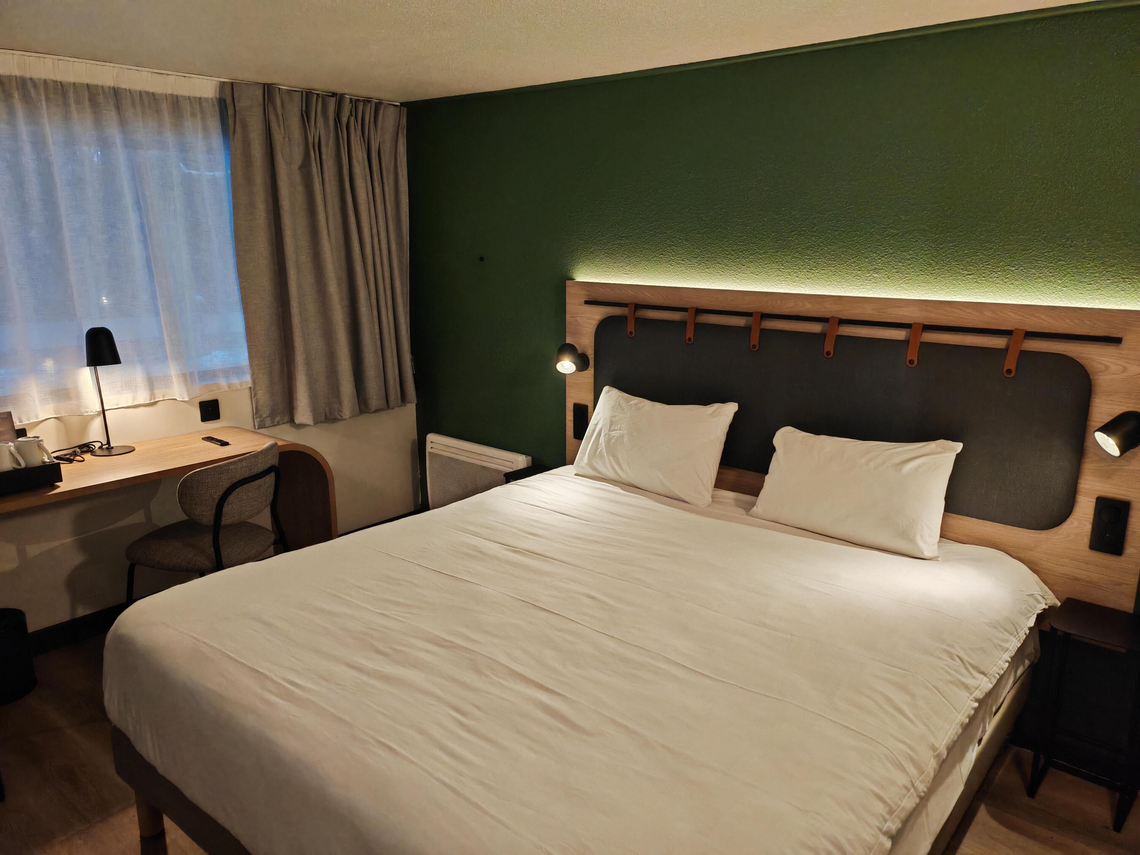 Une chambre d’hôtel équipée d’un lit, d’un bureau, d’une chaise, d’une lampe et offrant une vue sur l’extérieur.