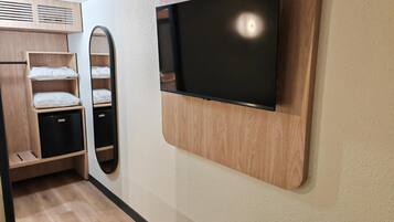A modern room with a built-in TV, wooden shelving, a mirror, and a compact storage unit.