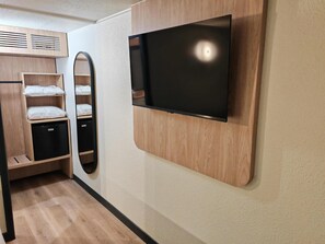 Une chambre moderne dotée d’un téléviseur encastré, d’étagères en bois, d’un miroir et d’un meuble de rangement compact.