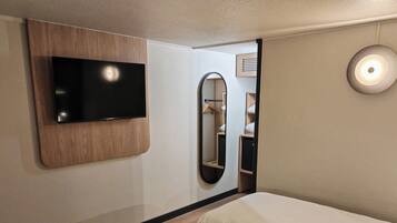 A hotel room with a mounted TV, a mirror, and a bedside lamp.