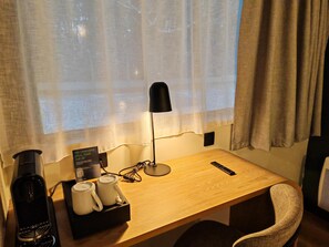 A hotel room with a wooden desk, a black desk lamp, a remote control, a coffee maker, and a tray with two white mugs. - Campanile Lille Sud Douai Cuincy (Cuincy)