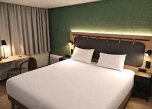 A neatly arranged hotel room with a large bed, a desk with a chair, a nightstand with a lamp, and a headboard with a light fixture. - Campanile Lille Sud Douai Cuincy (Cuincy)
