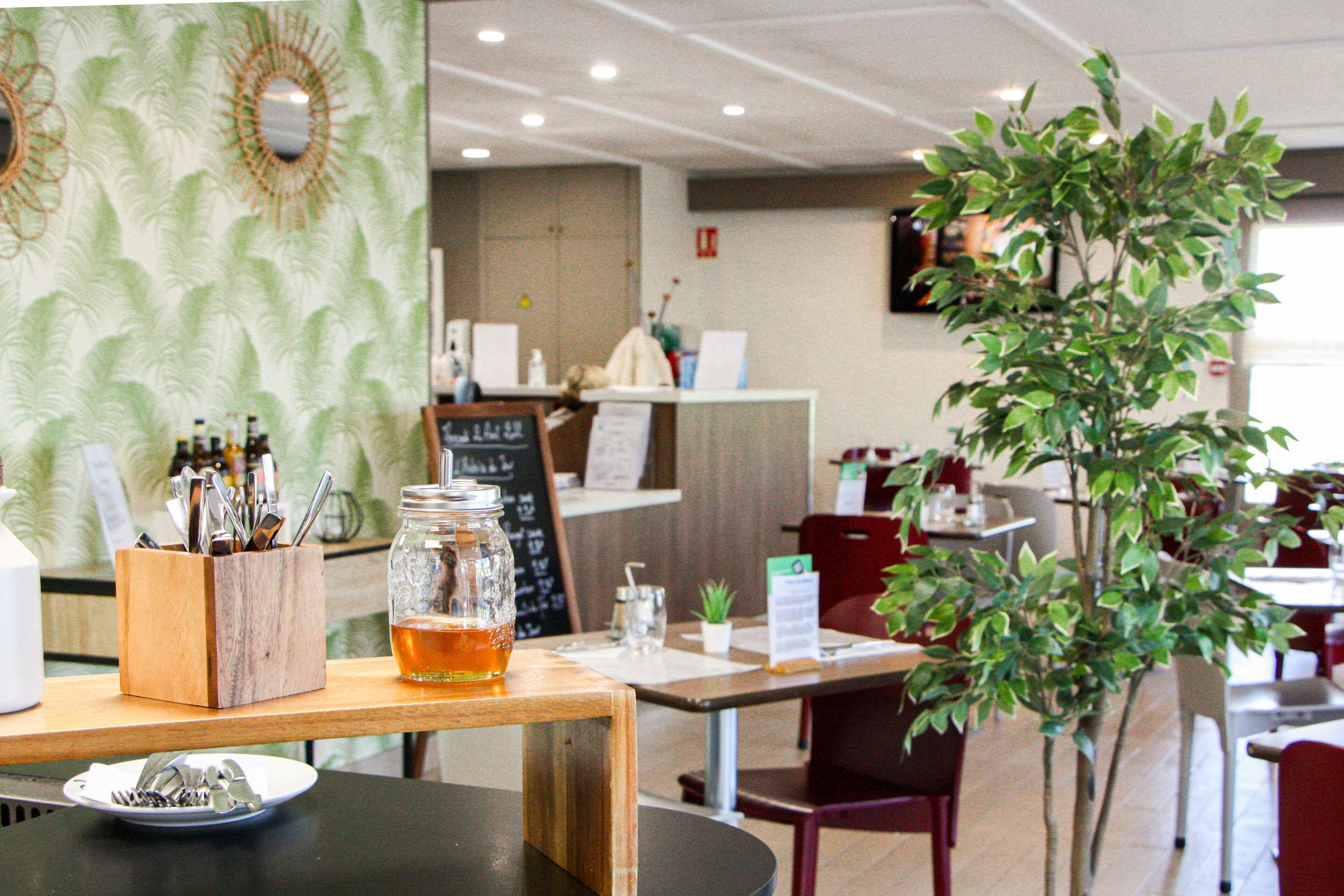 A restaurant interior with a wooden table, a glass jar with a beverage, and a menu board.