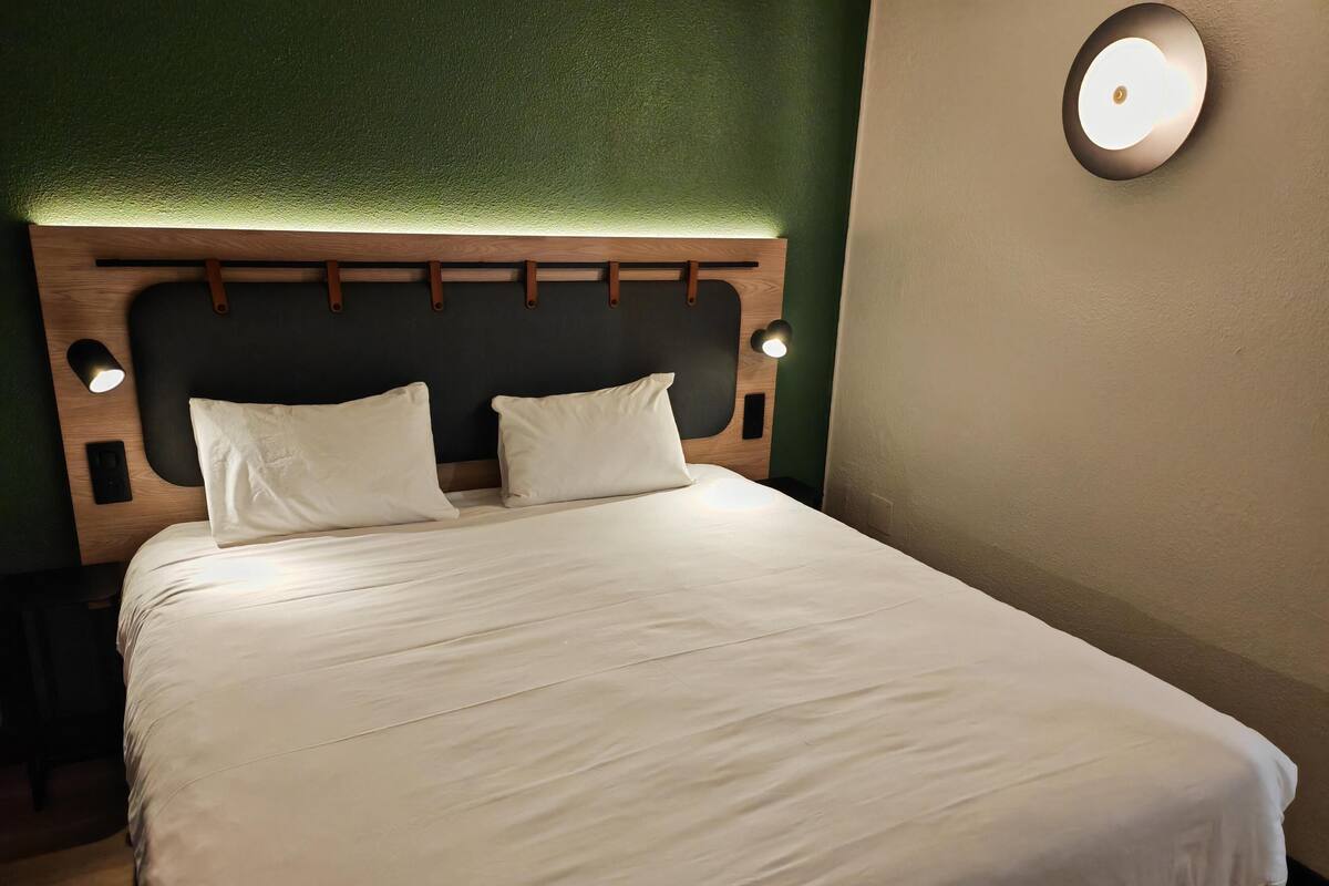A neatly made bed with a wooden headboard, two pillows, and a wall-mounted light fixture.