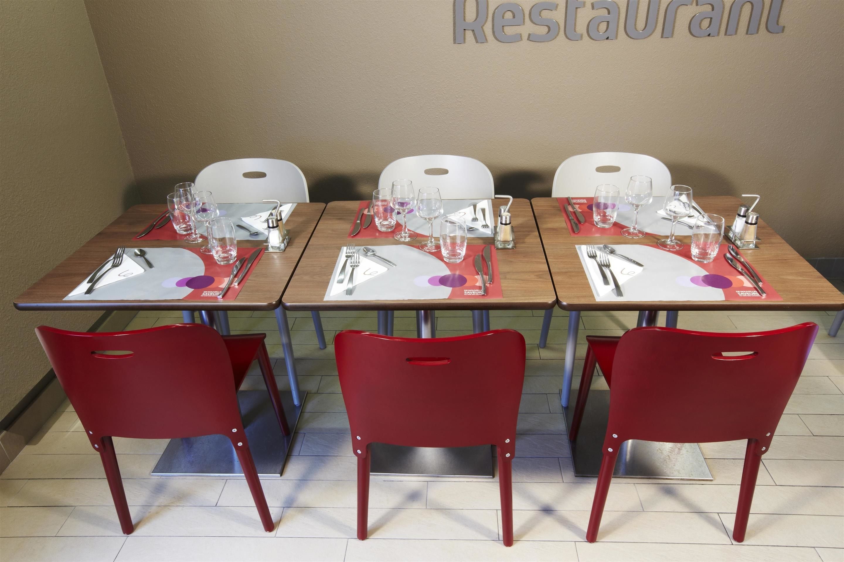A restaurant table set with red chairs, white plates, cutlery, and glasses.