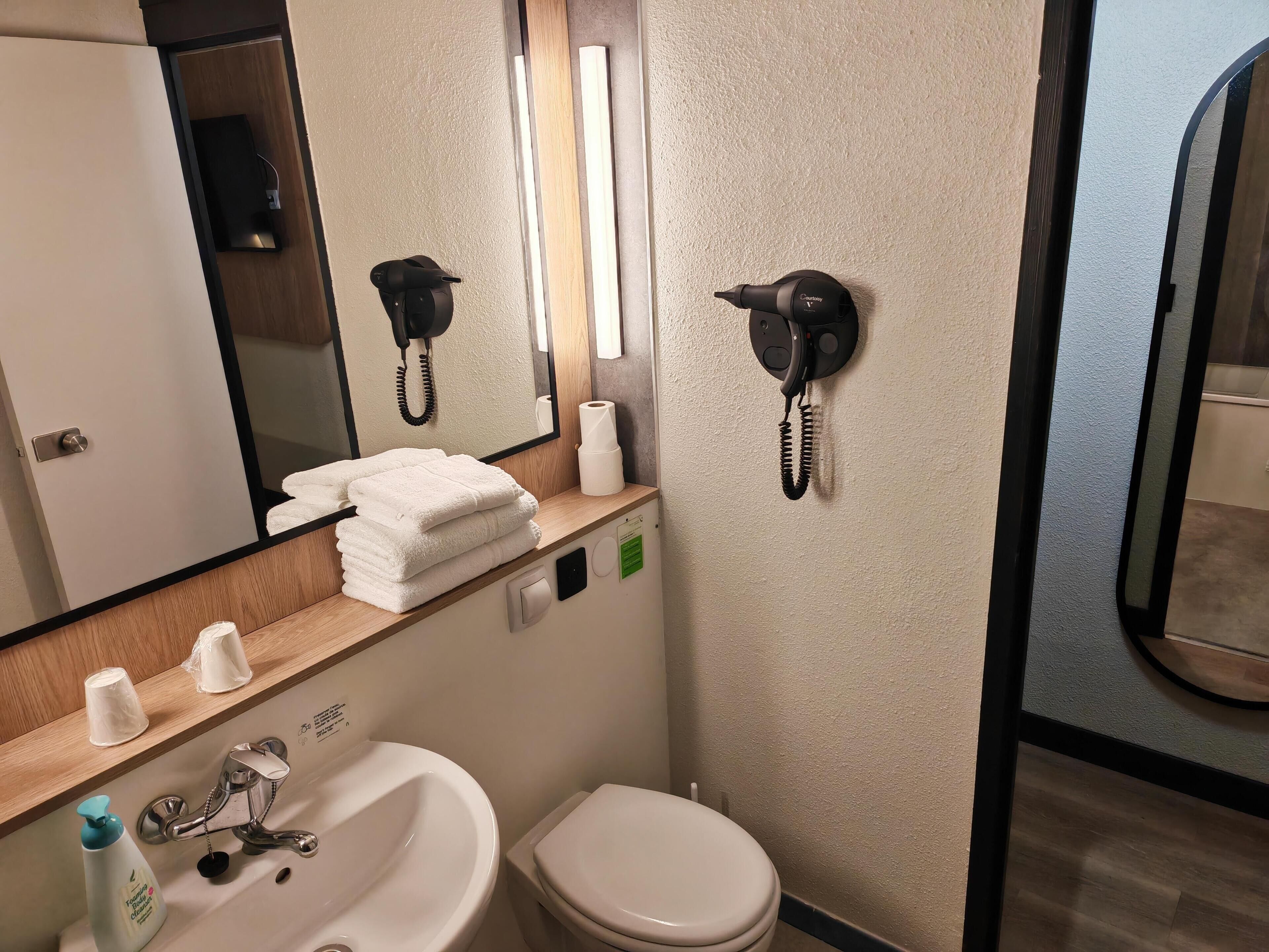 Un baño de hotel con lavamanos, inodoro, espejo, toallero y teléfono.