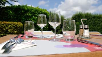 A table set with wine glasses, cutlery, and salt and pepper shakers, with a view of greenery and a clear sky in the background.