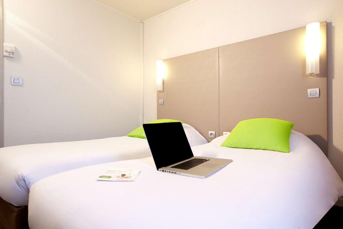 A hotel room with two beds, a laptop on one bed, and a brochure on the bed.