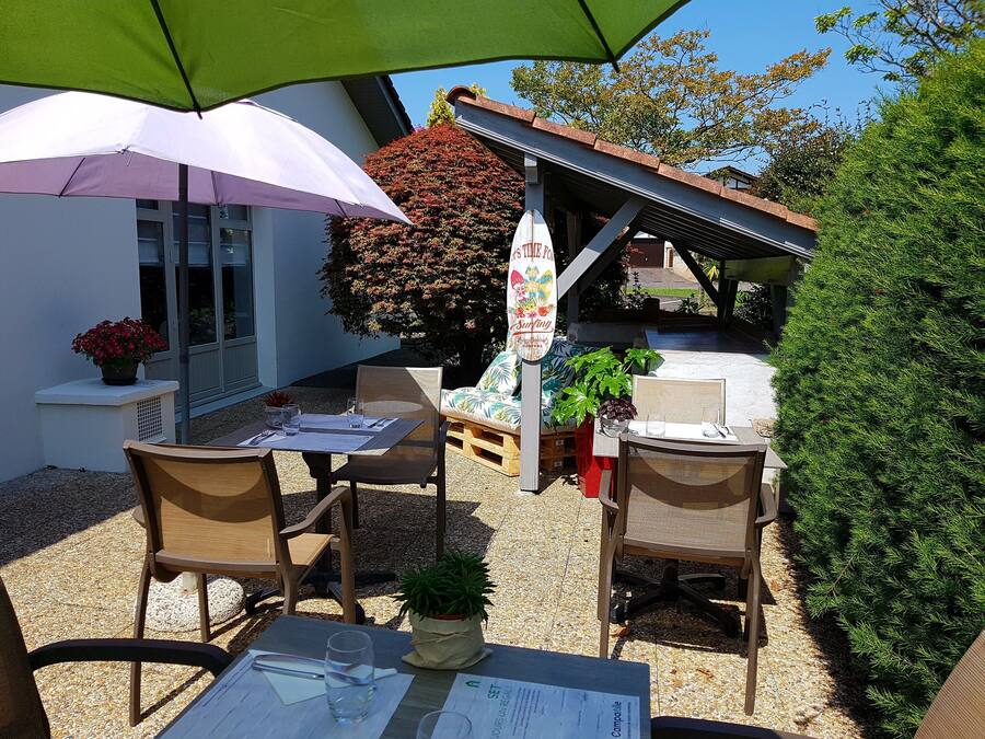 Una terrazza esterna con tavoli e sedie, un ombrellone verde e un cartello con scritto 'Surfing'.