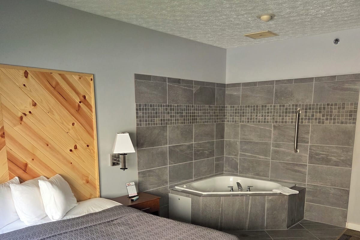 A hotel room with a large bed, a separate bathroom with a bathtub, and a wooden headboard.