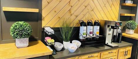 A modern kitchen with wooden cabinetry, a herringbone-patterned backsplash, and a coffee station with a coffee machine and dispensers.