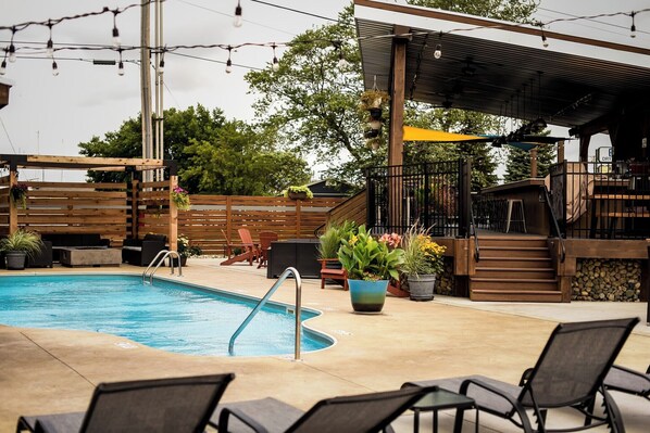 Un área de piscina con sillones de descanso, una terraza de madera y un espacio de estar cubierto.