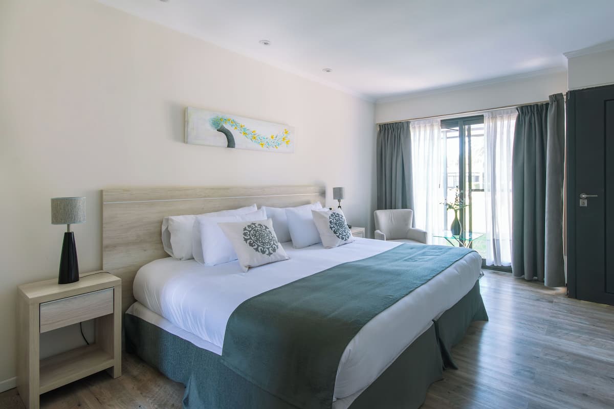 A modern bedroom with a large bed, a bedside table with a lamp, a chair, and a painting on the wall.