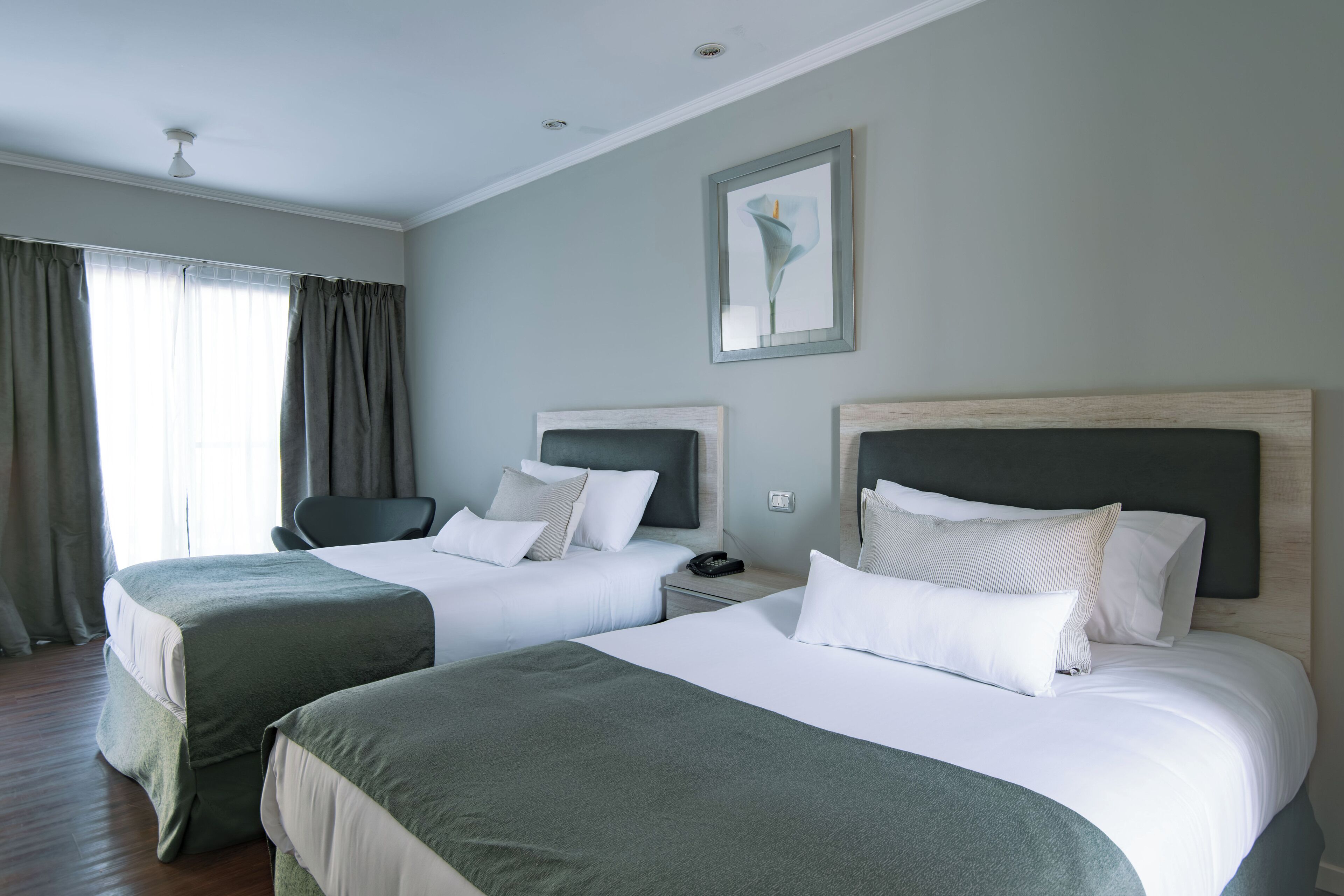 Habitación de hotel con dos camas, una silla, una mesita de noche y un cuadro en la pared.