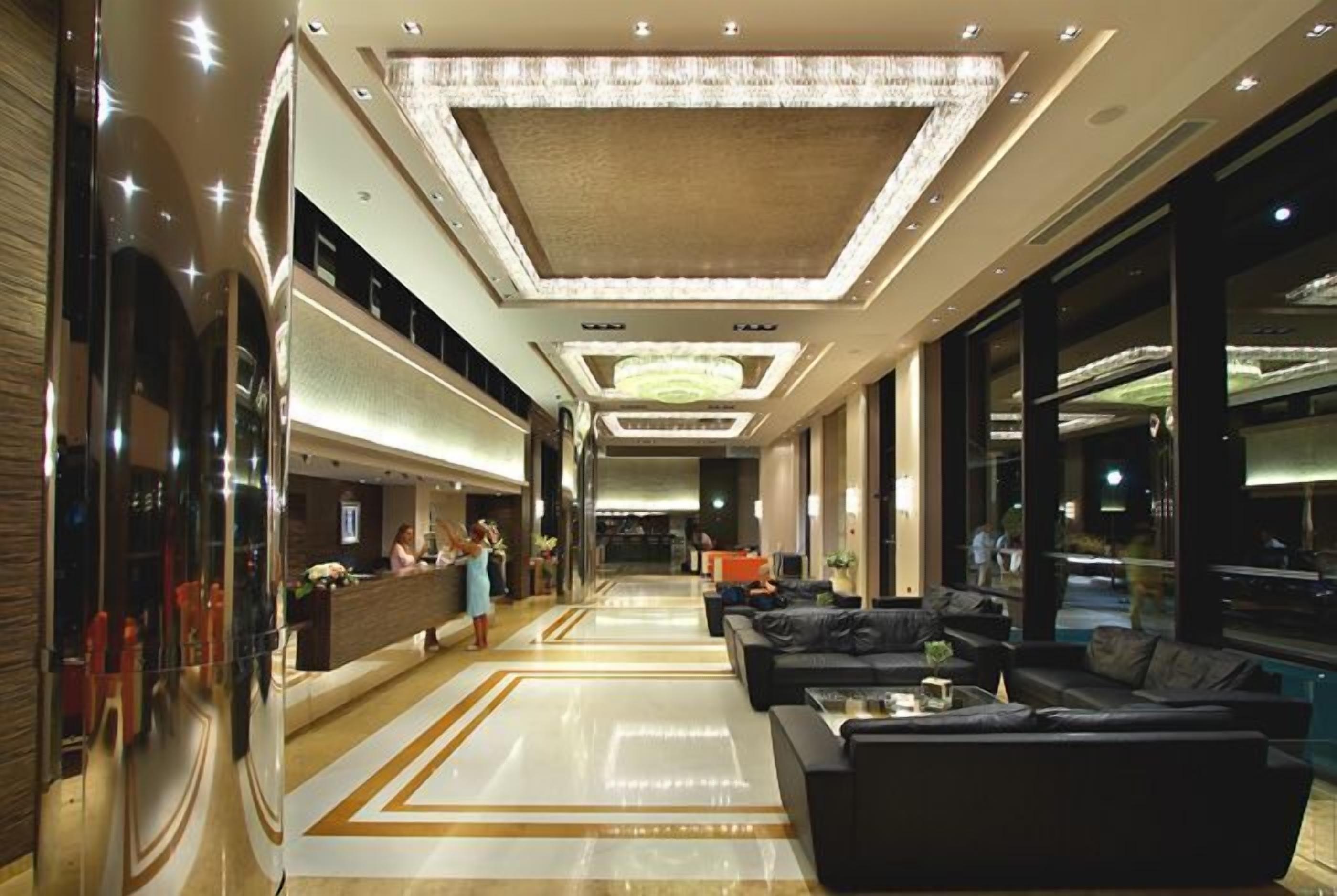 Een moderne hotellobby met een receptiebalie, een zithoek en grote ramen.