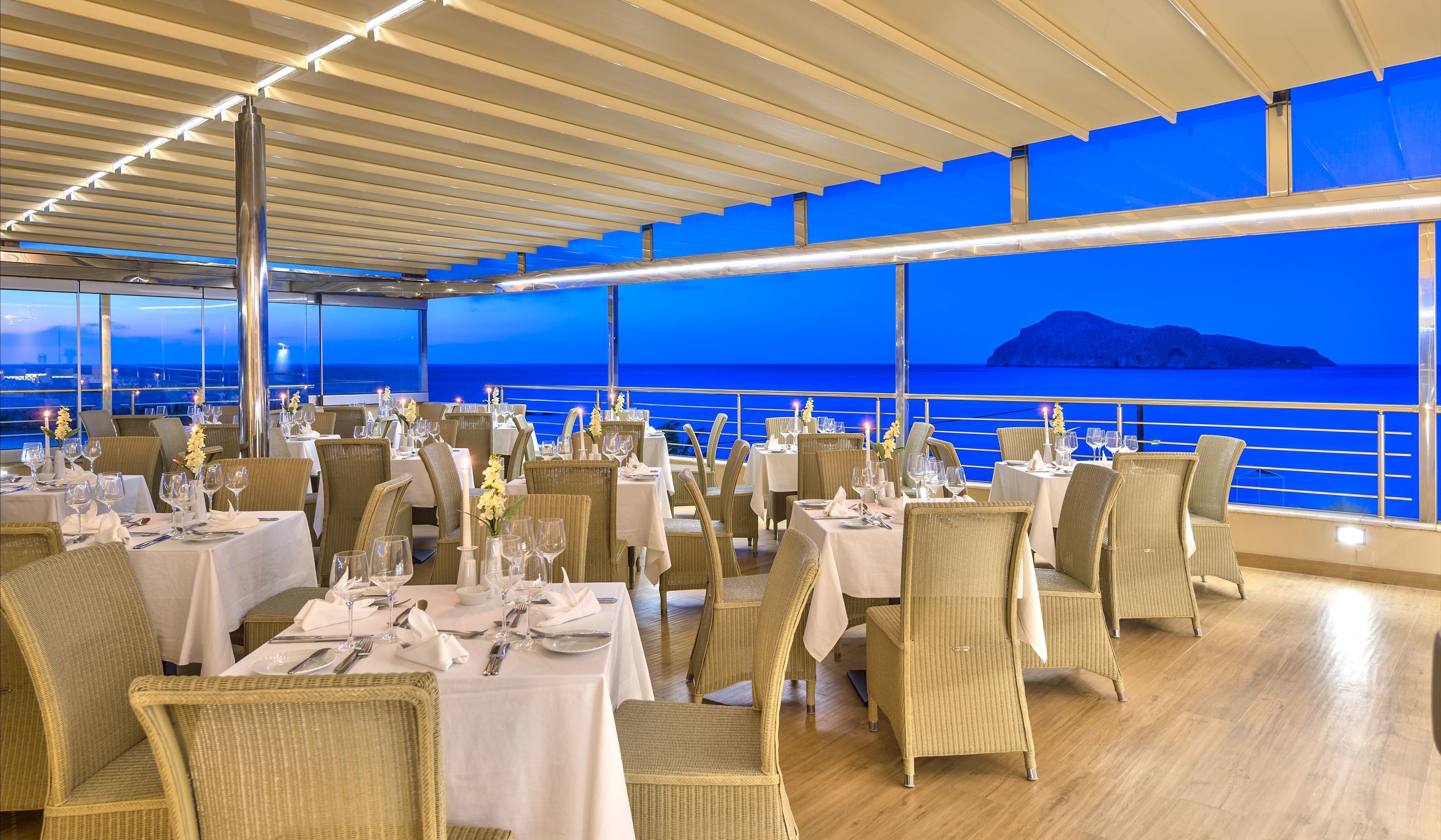 Un restaurante con mesas dispuestas para comer, sillas de mimbre y vistas al mar.