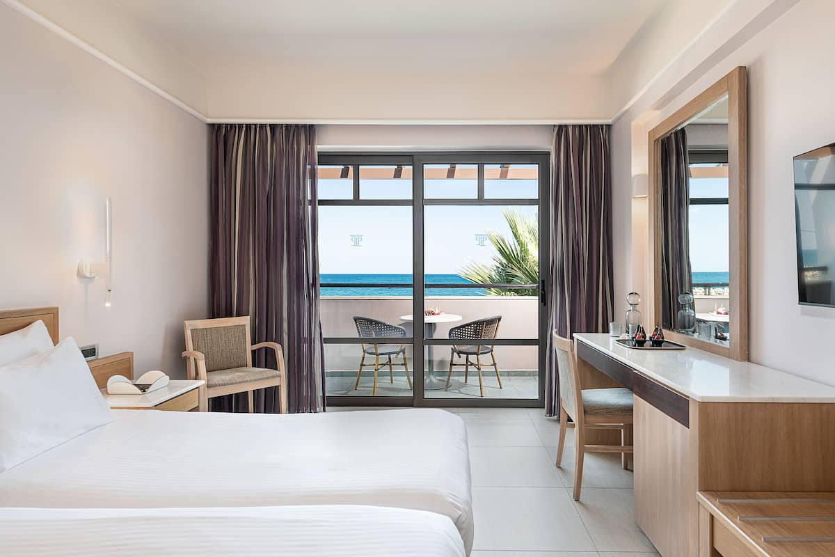 Ein Hotelzimmer mit Bett, Schreibtisch, Stuhl und einem Balkon mit Meerblick.
