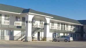 Un edificio de dos pisos con un atrio central, varios balcones y un estacionamiento con automóviles.