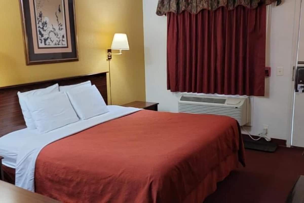 A hotel room with a bed, two bedside lamps, a wall-mounted air conditioner, and a door.