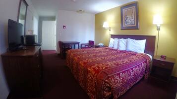 A hotel room with a large bed, a desk, a chair, a television, and a bedside table.