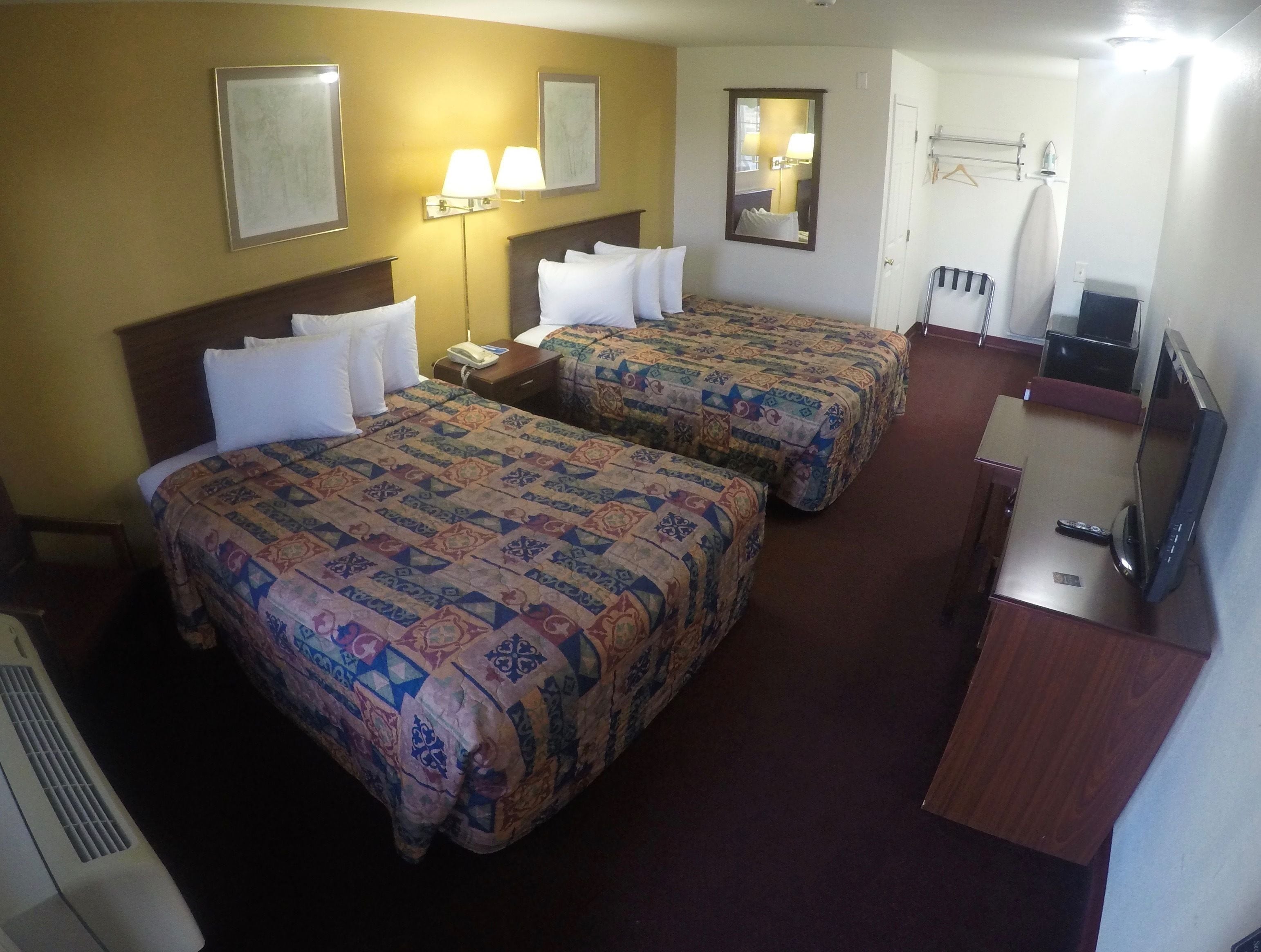 A hotel room with two beds, a desk, a TV, and a mirror.
