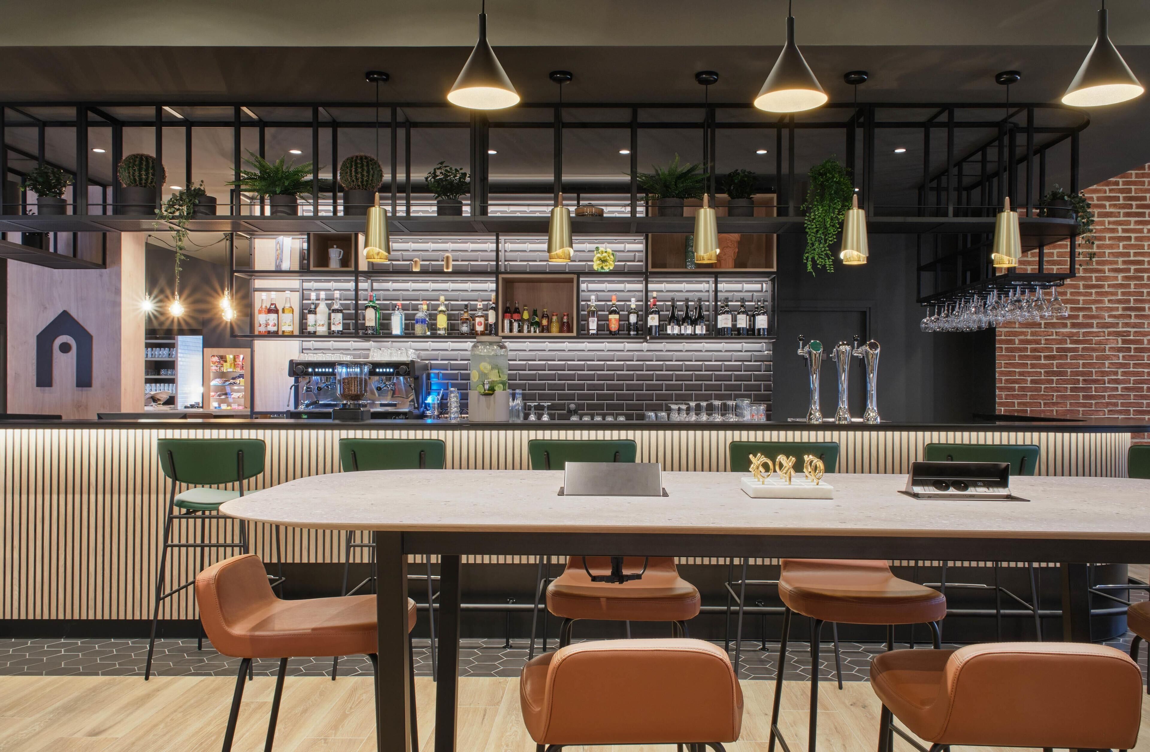 A modern bar area with a brick wall, hanging pendant lights, and a variety of bottles and glasses on shelves.