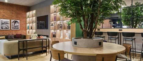 A modern interior with a round wooden table, chairs, a brick wall, and a large tree planter.