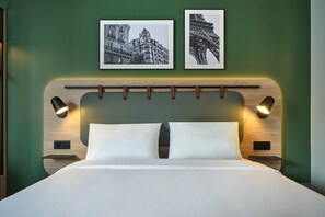 Une chambre d’hôtel avec un lit, deux cadres photos accrochés au mur et des lampes de chevet.
