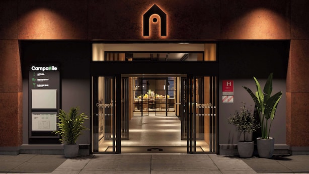 L'entrée d'un hôtel au design moderne, avec une porte en verre, un comptoir d'accueil et des plantes en pot.