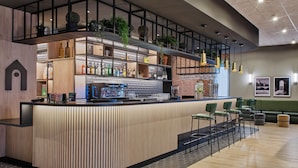 Un espace bar moderne, doté d’un comptoir, de sièges et d’étagères où sont exposées des bouteilles.