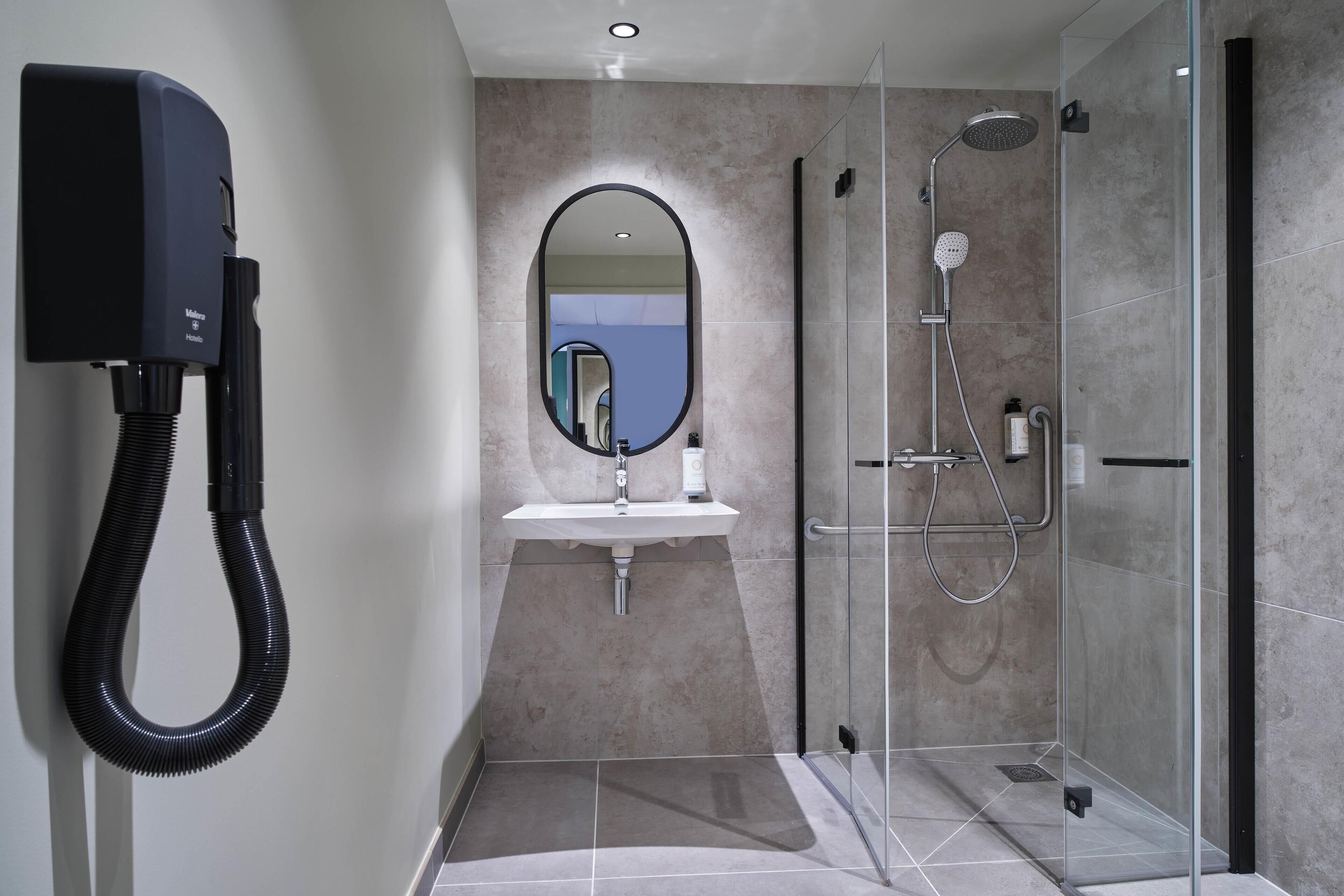 A modern bathroom with a handheld vacuum, a sink with a mirror, and a glass-enclosed shower.