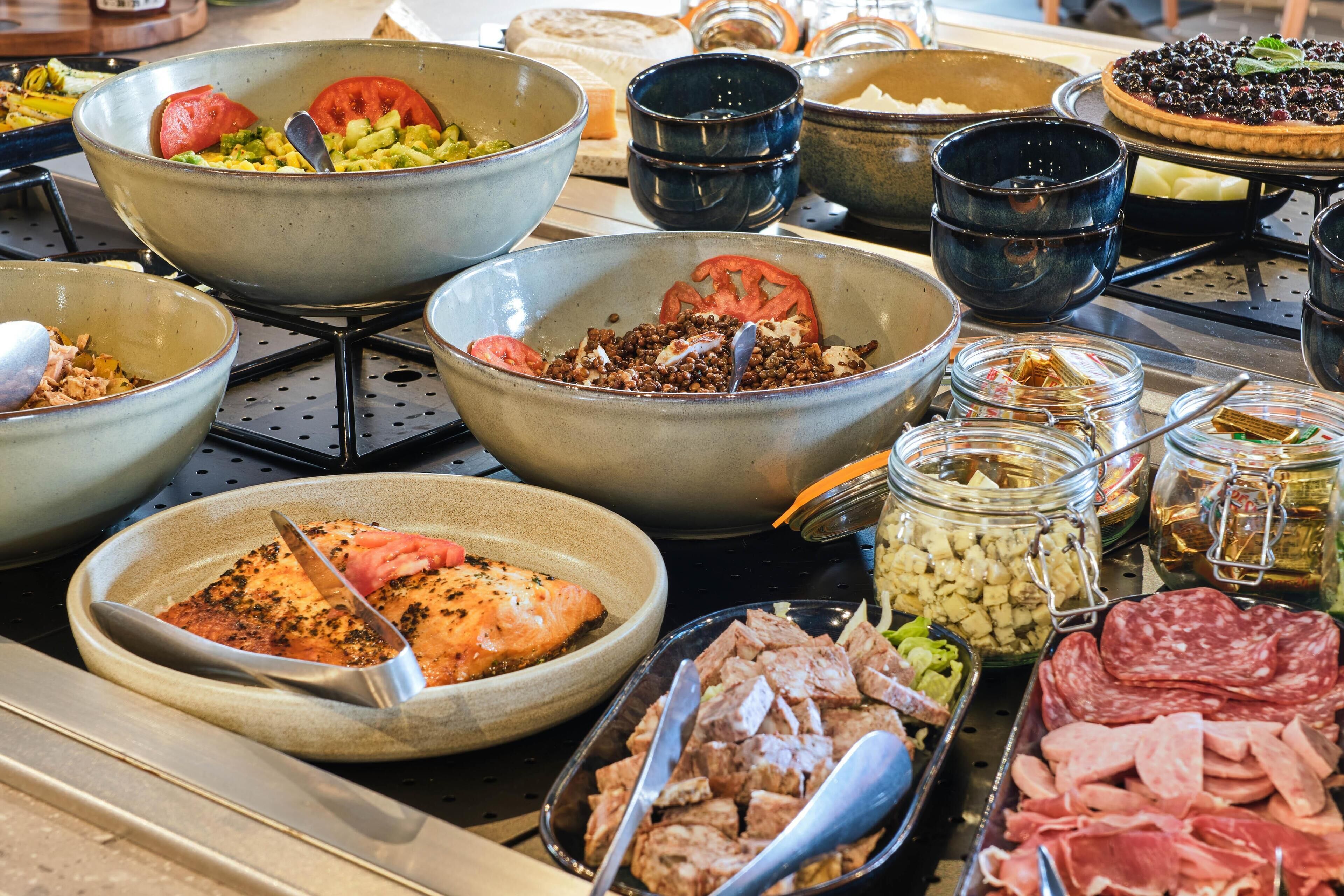 Un buffet proposant une variété de plats, notamment des salades, un plat de saumon et des plateaux de viandes.